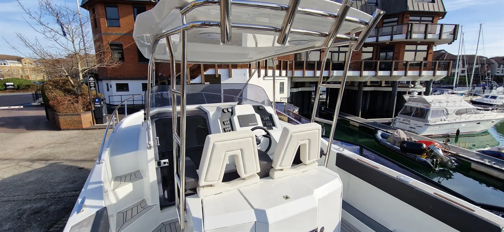 Pilot seat and controls of a white motorboat docked near luxury homes and other vessels in a marina.